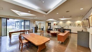 A spacious room with a large wooden table and chairs, a reception desk, and framed artwork on the walls. - BENIKEA Yufuin Kinrinko Hotel Museum (Yufuin)