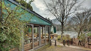 A restaurant with outdoor seating overlooking a lake, surrounded by trees and mountains. - BENIKEA Yufuin Kinrinko Hotel Museum (Yufuin)