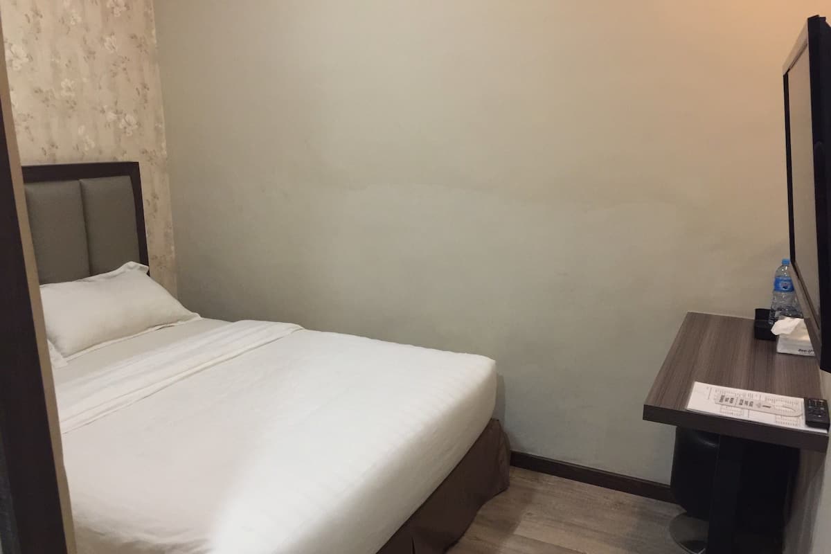Een hotelkamer met een bed, een klein bureau, een prullenbak en een waterfles.