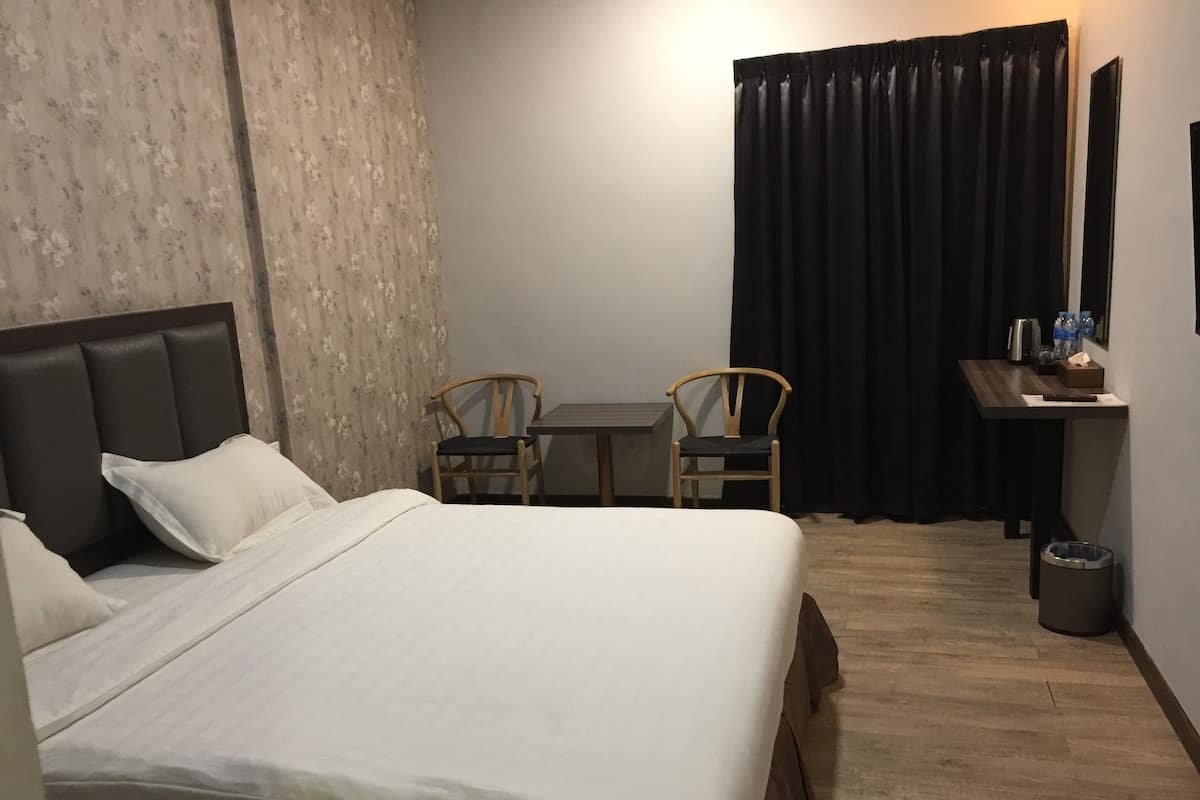 Een hotelkamer met een groot bed, twee houten stoelen, een kleine tafel, een bureau met een spiegel en een prullenbak.