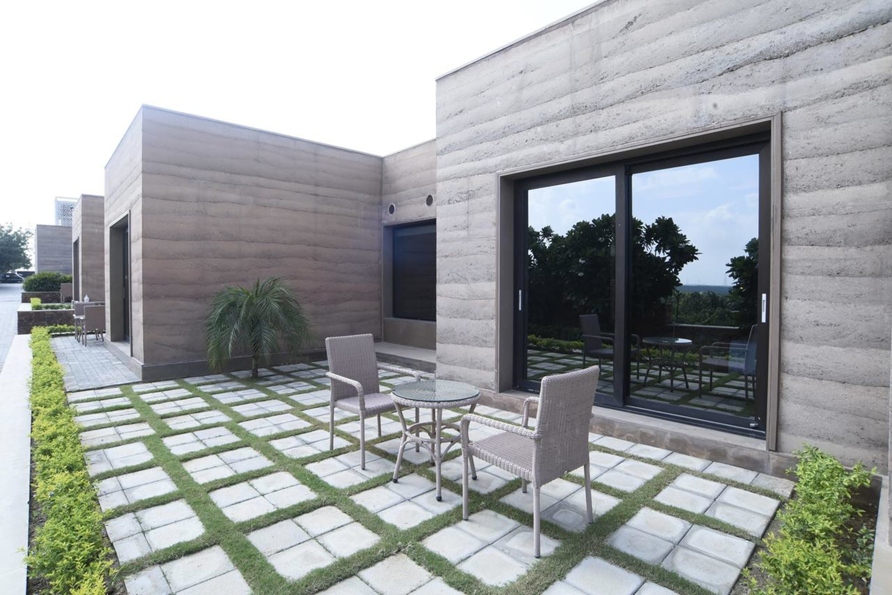 A modern building with a concrete facade, large sliding glass doors, and a paved patio with a small table and chairs.