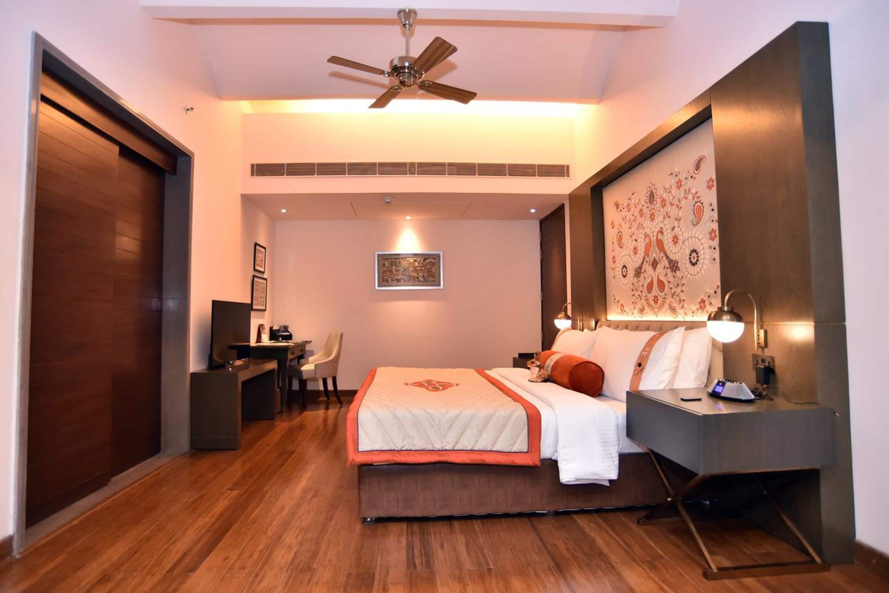 A modern hotel room with a large bed, a desk, a chair, and a ceiling fan.