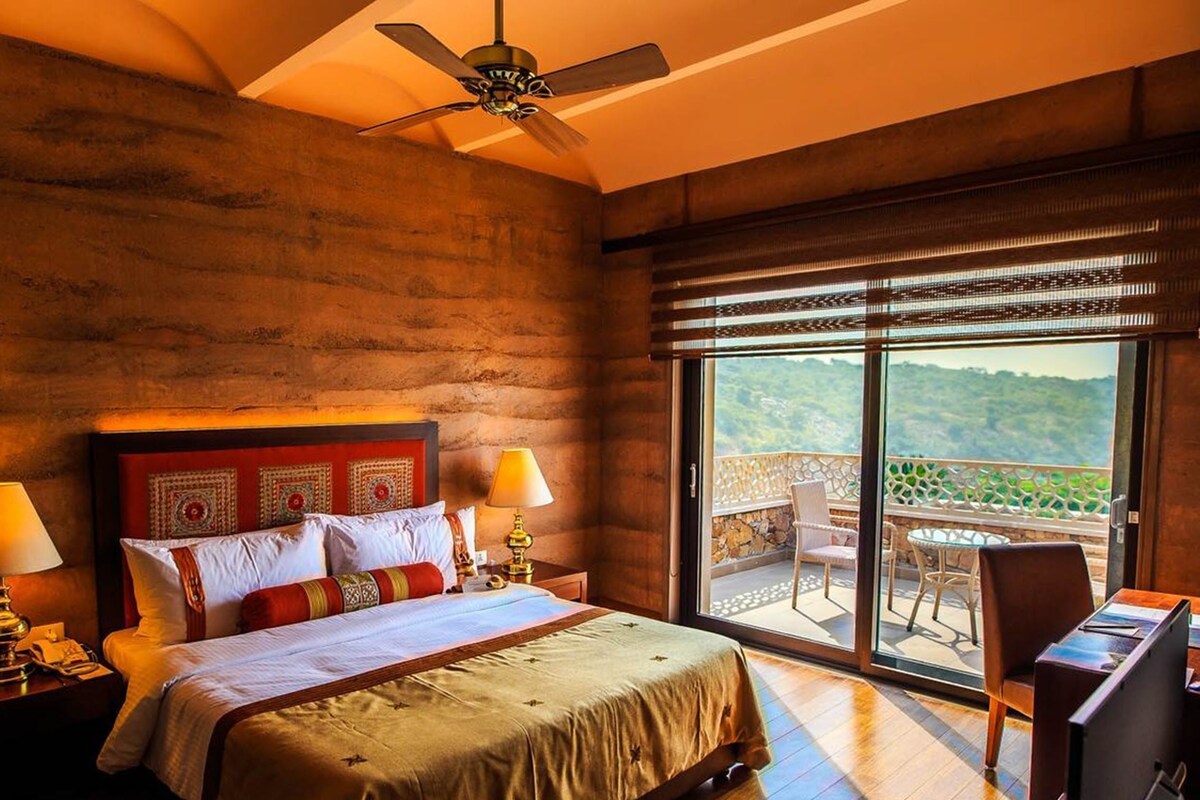 A bedroom with a large bed, two bedside lamps, a ceiling fan, and a balcony with a view.