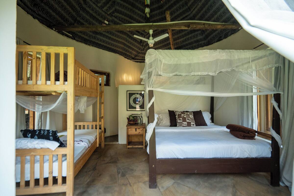 Ein Zimmer mit einem Holzbett, einem Einzelbett mit Baldachin, einem kleinen Nachttisch und einem an der Wand befestigten Regal.