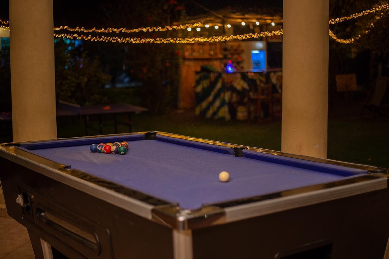 Una mesa de billar con bolas, rodeada de pilares y luces colgantes, que denota un área recreativa interior.