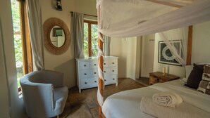 Ein Schlafzimmer mit einem Bett, einem Sessel, einer Kommode, einem Nachttisch, einem Spiegel und einem Fenster mit Vorhängen.