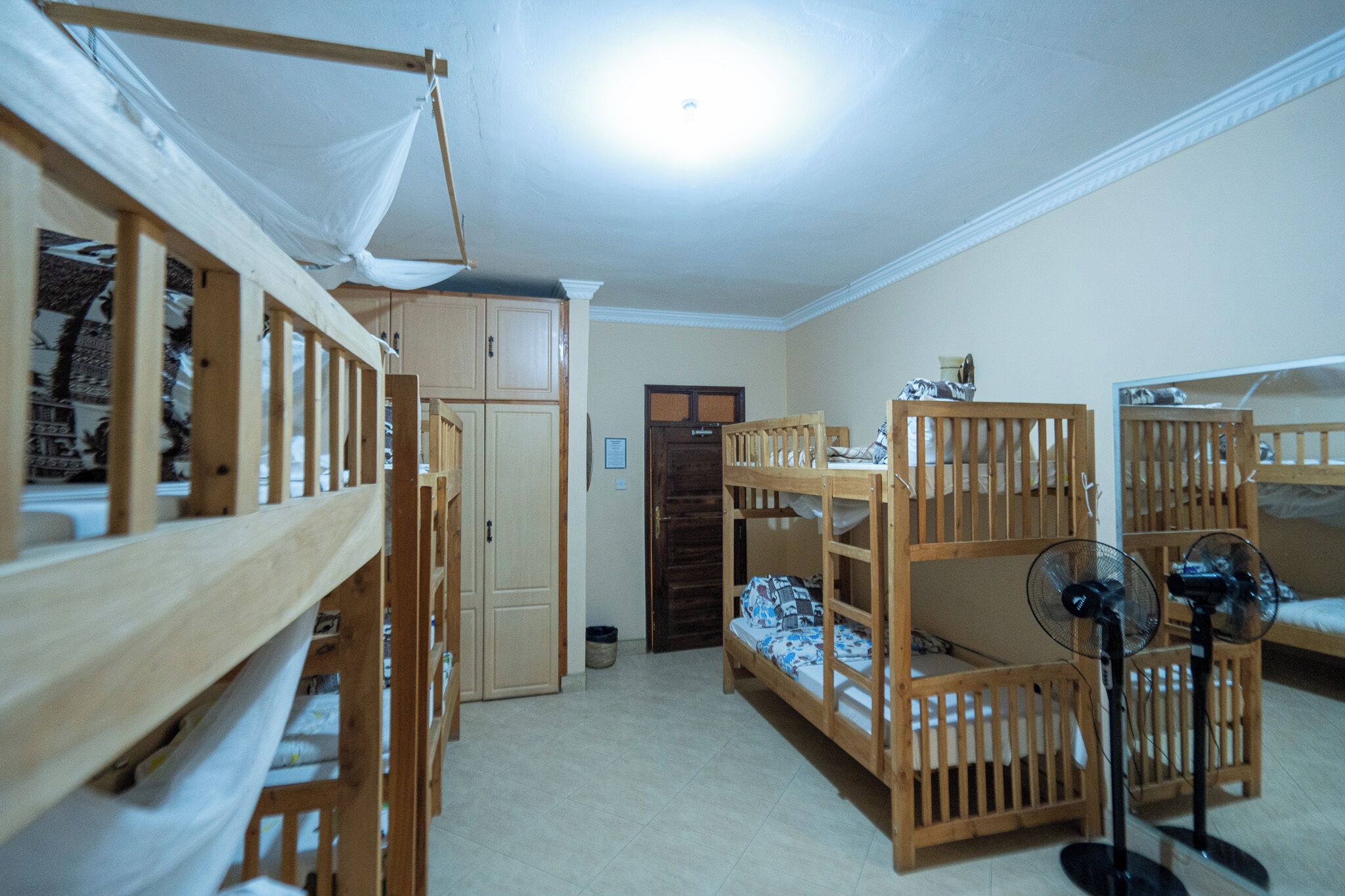 Ein Schlafsaalzimmer mit Etagenbetten, einem Kleiderschrank, einer Tür und einem Ventilator.