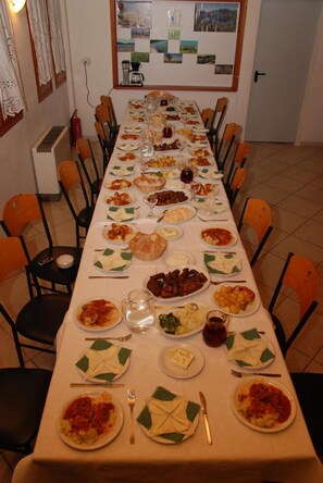 A long dining table set with various dishes, surrounded by chairs. - Antigoni Hotel (Lake Plastiras)
