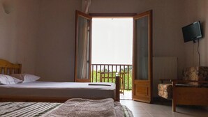 Un dormitorio con cama, una silla, televisión y puerta abierta que da a un balcón.