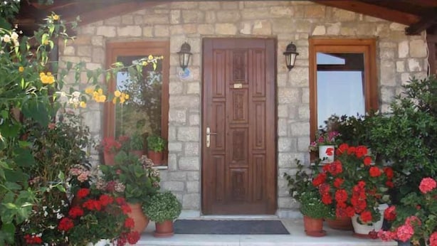 Un edificio de piedra con puerta de madera y dos ventanas, rodeado de macetas con plantas y flores.