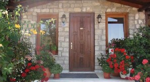 Un bâtiment en pierre avec une porte en bois et deux fenêtres, entouré de plantes et de fleurs en pot.