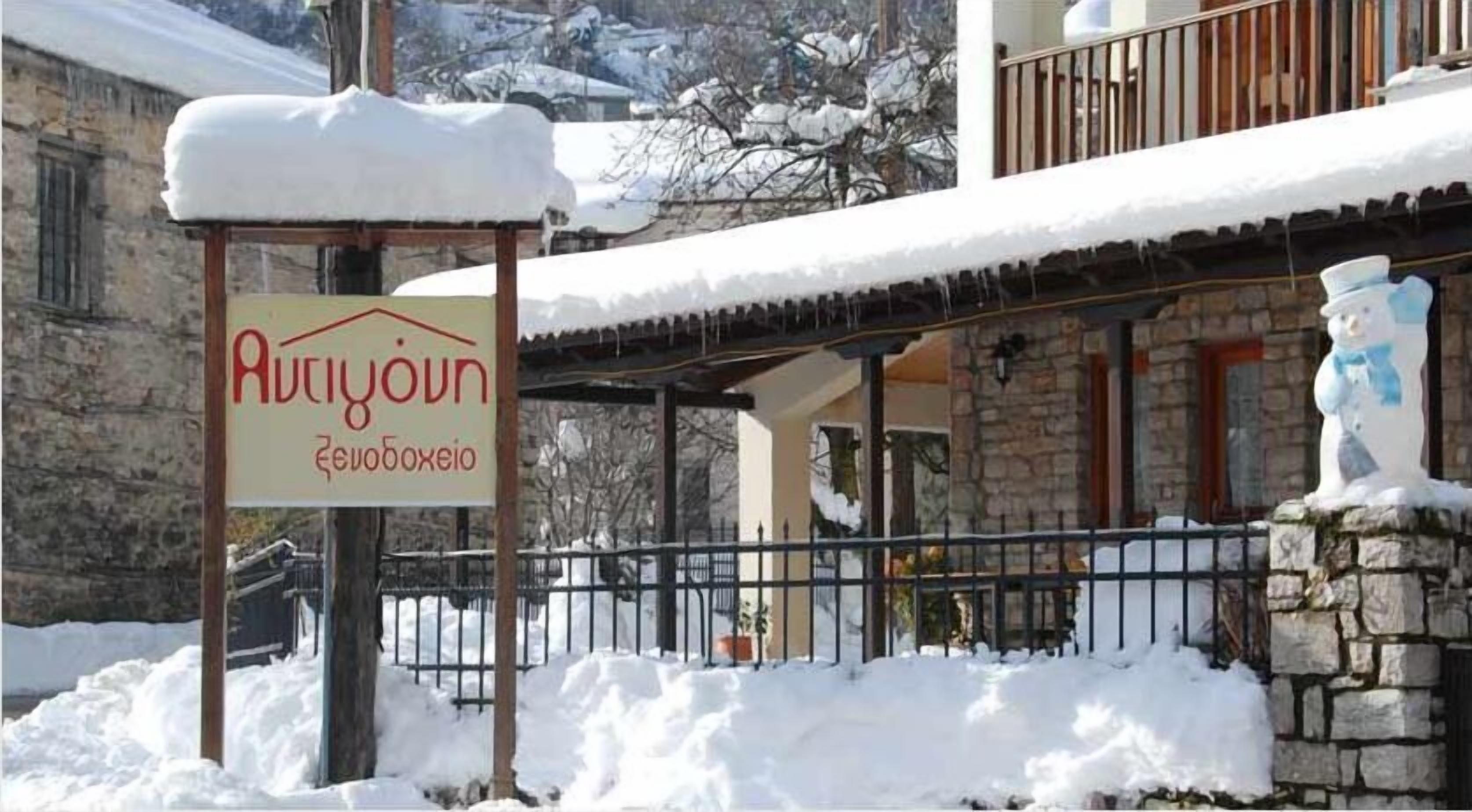 A sign for a hotel named "Ariyoun" with a stone building in the background covered in snow.