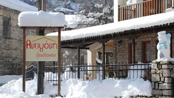 A sign for a hotel named "Ariyoun" with a stone building in the background covered in snow.
