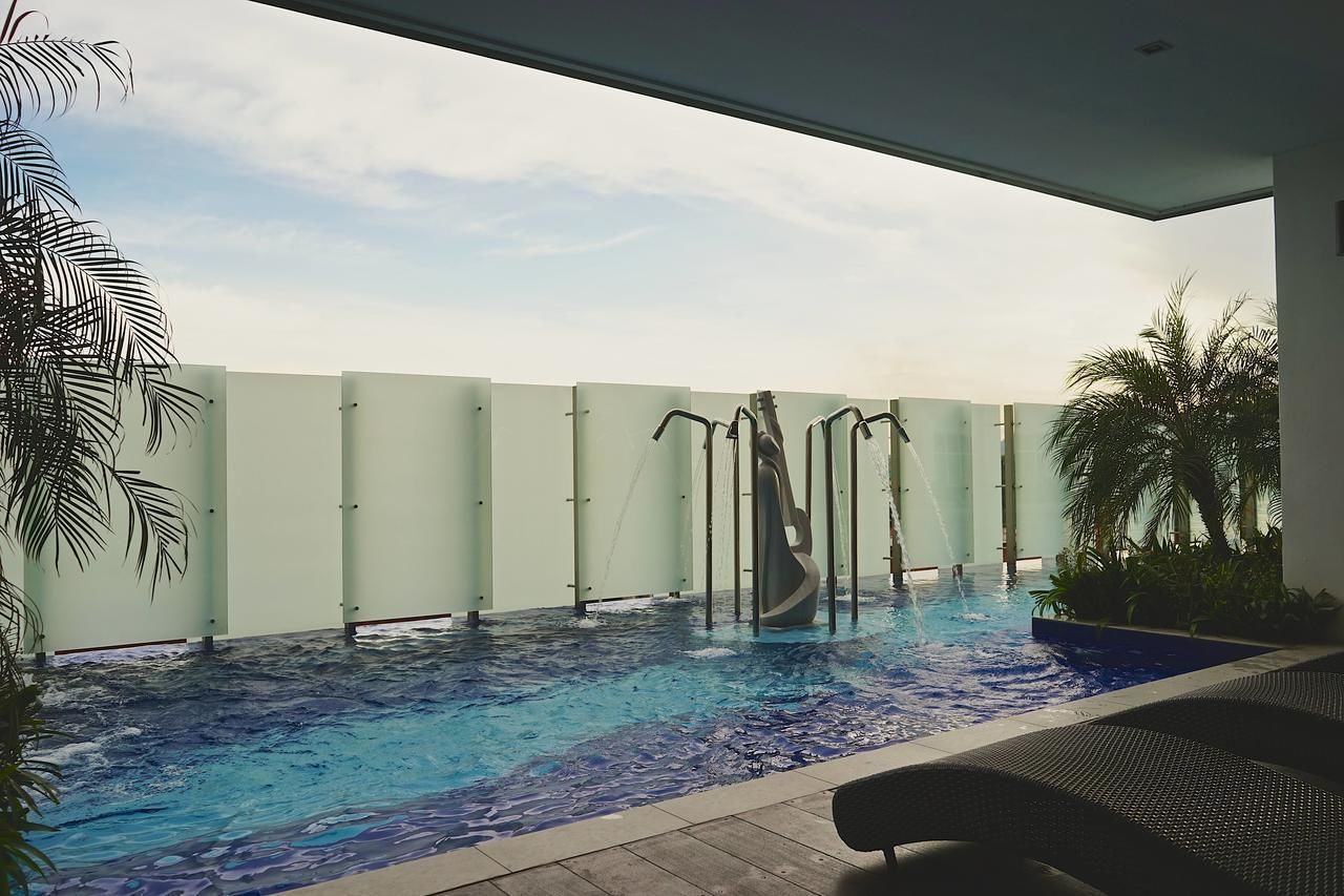 An indoor swimming pool with a water slide, surrounded by palm trees and a glass partition.
