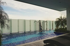 An indoor swimming pool with a water slide, surrounded by palm trees and a glass partition.