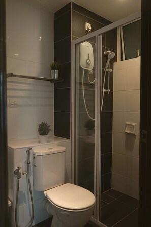 A modern bathroom with a toilet, a shower enclosure, and a small shelf with a plant.