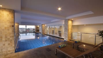 Una piscina interior con pared de vidrio, sillones de descanso y vistas de la ciudad.