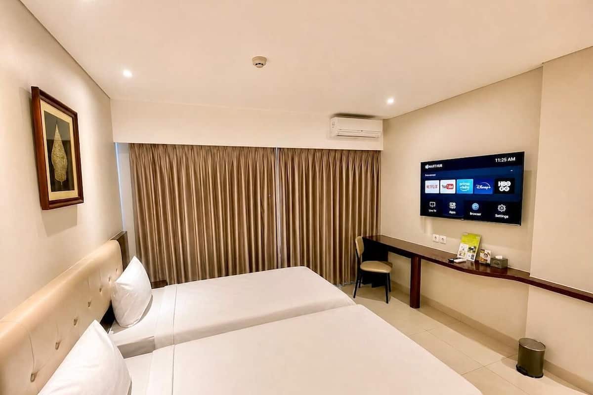 A hotel room with a bed, a desk, a chair, an air conditioning unit, a television, and a window with curtains.