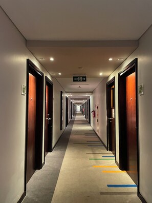 A hotel corridor with doors on both sides, a carpet with colorful lines, and an exit sign overhead. - Hotel PrimeBiz Tegal (Tegal)