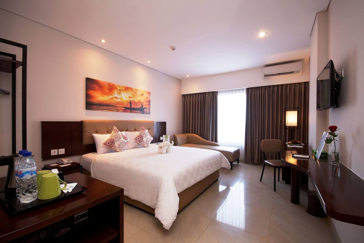 A hotel room with a large bed, a desk, a chair, a TV, and a painting on the wall.