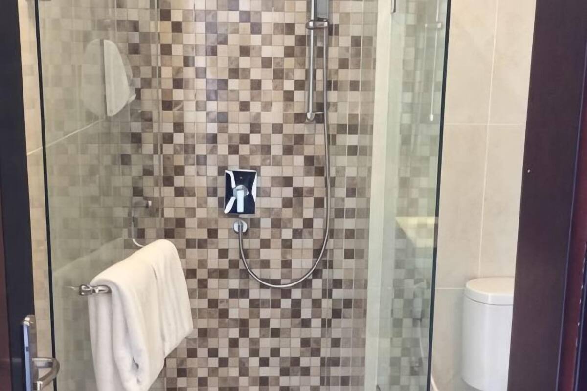 A glass-enclosed shower with a checkered tile wall, a handheld showerhead, and a towel hanging on the door.
