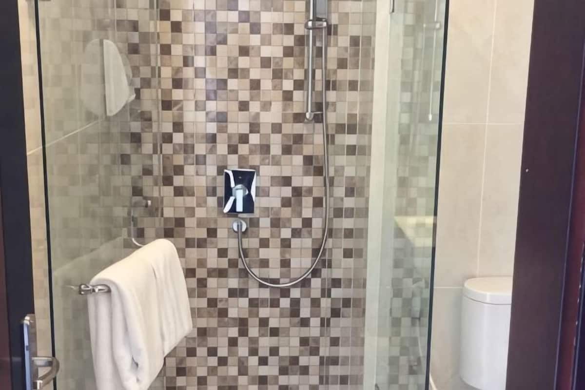 A glass-enclosed shower with a checkered tile wall, a handheld showerhead, and a towel hanging on the door.