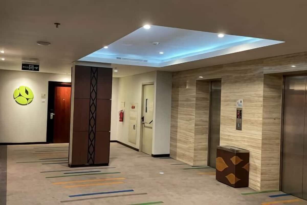 A hotel lobby with a reception desk, elevators, a fire extinguisher, and a large smiley face decoration on the wall.