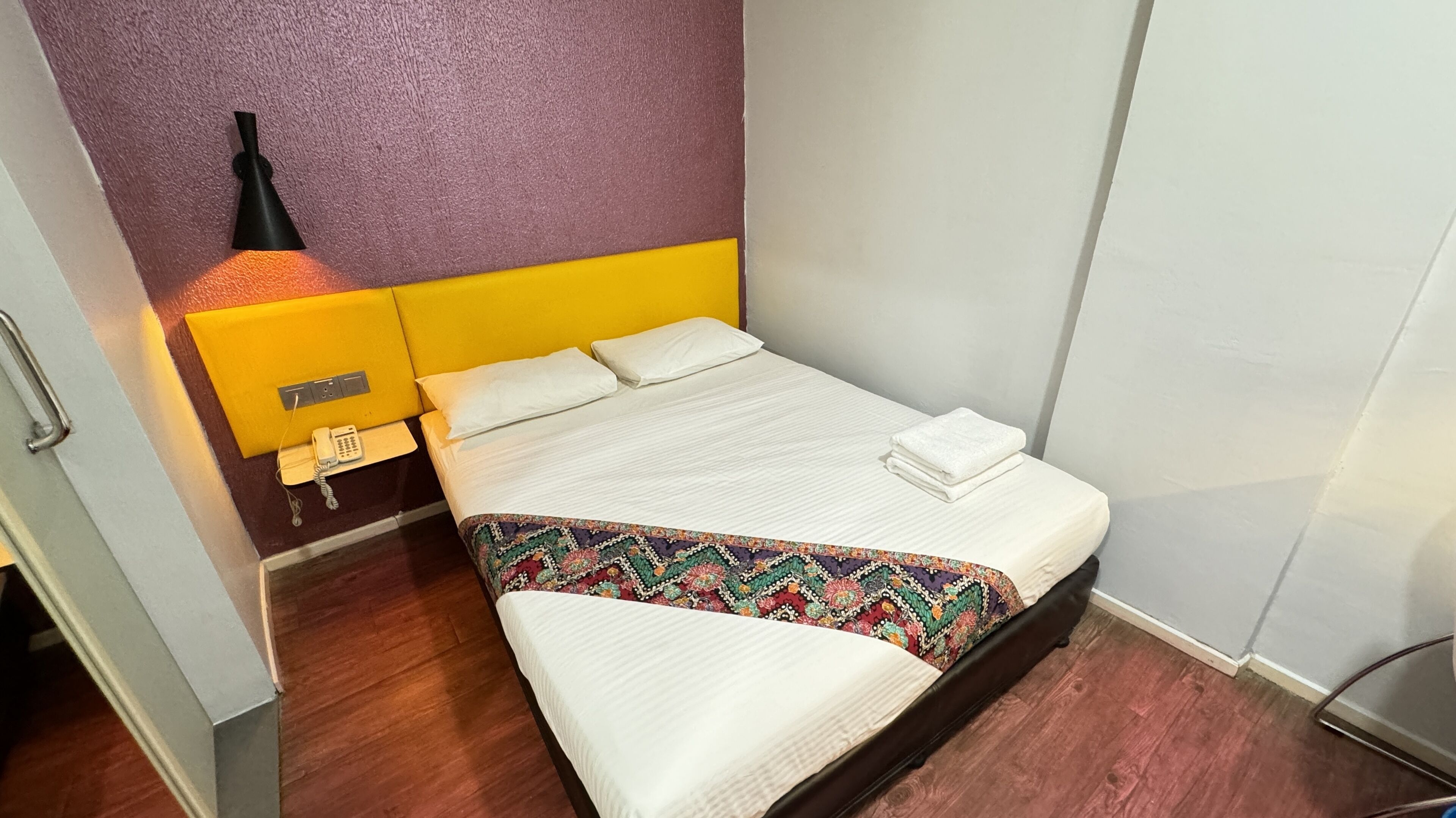 Una habitación de hotel con una cama, una mesita de noche con lámpara y un teléfono.