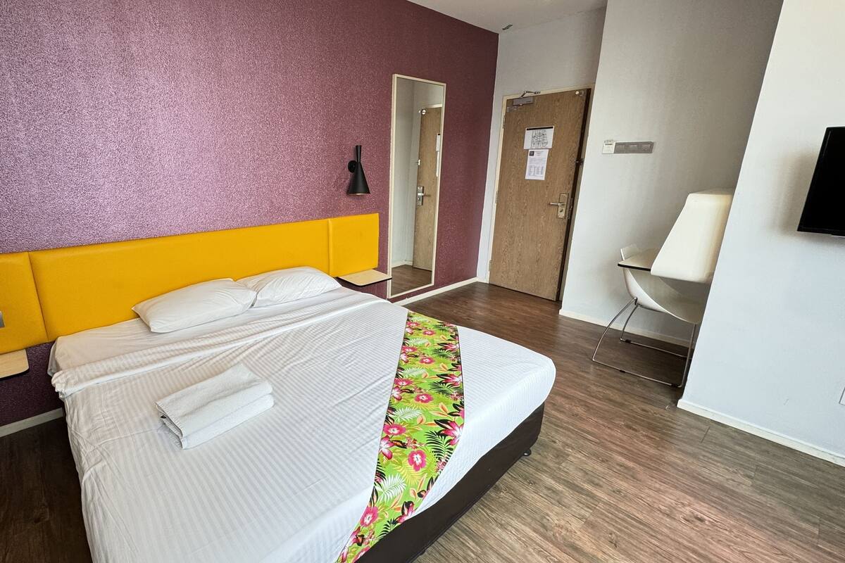 A hotel room with a bed, a telephone, a mirror, a desk, and a chair.