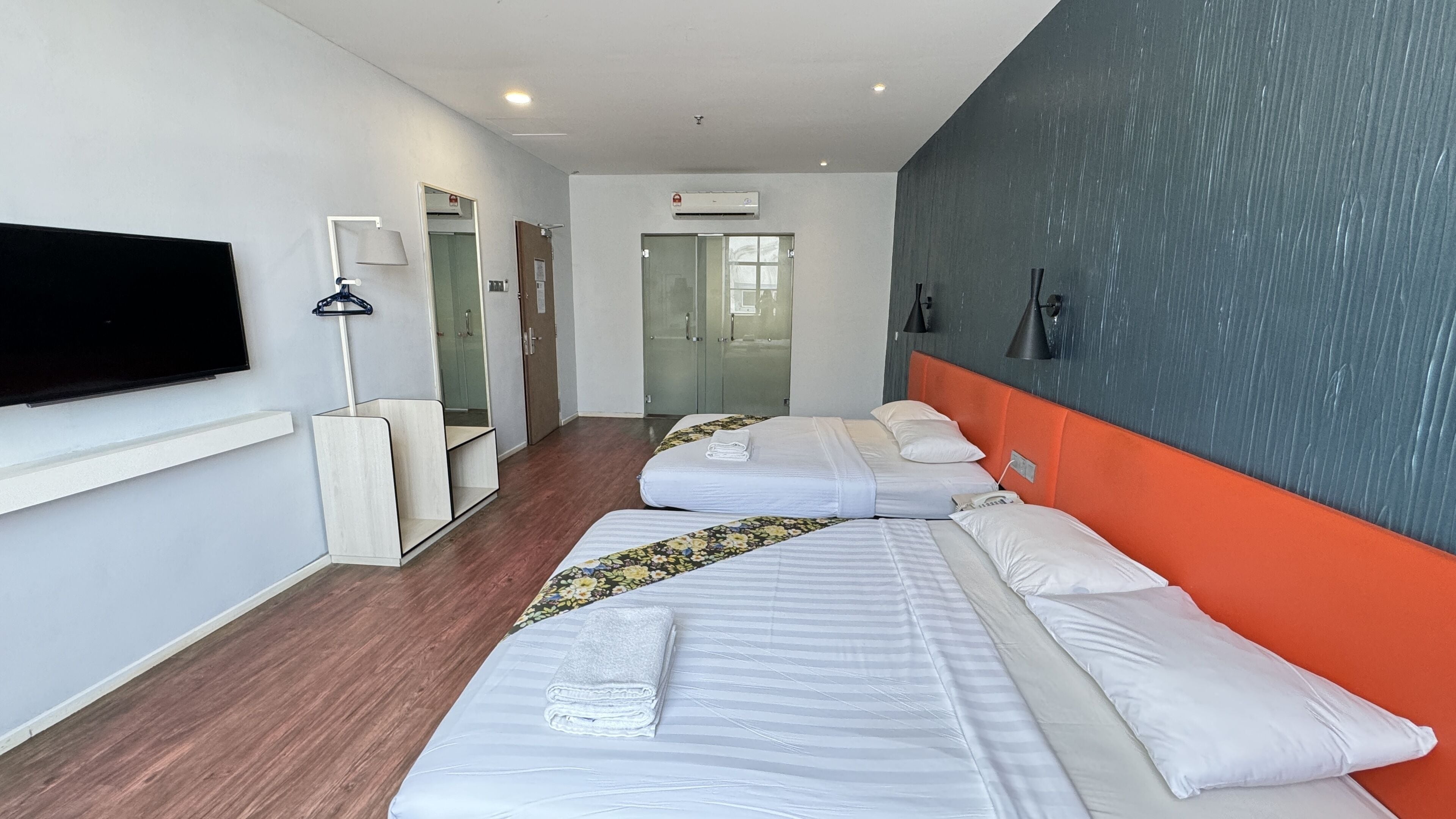 A hotel room with two beds, a TV, a wardrobe, and a mirror.