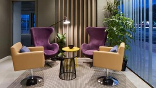 Un área de descanso moderna con dos sillones morados, una mesita redonda y una lámpara de pie.
