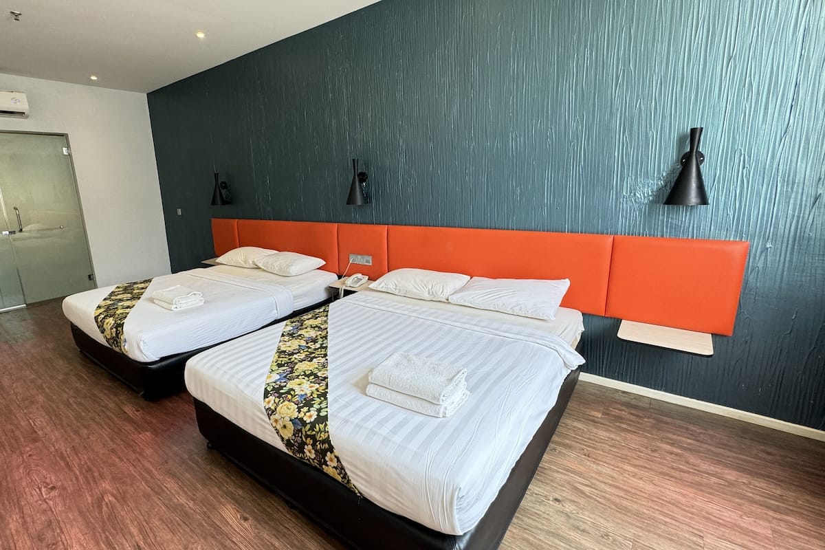 Habitación de hotel con dos camas, una pared oscura y suelo de madera.
