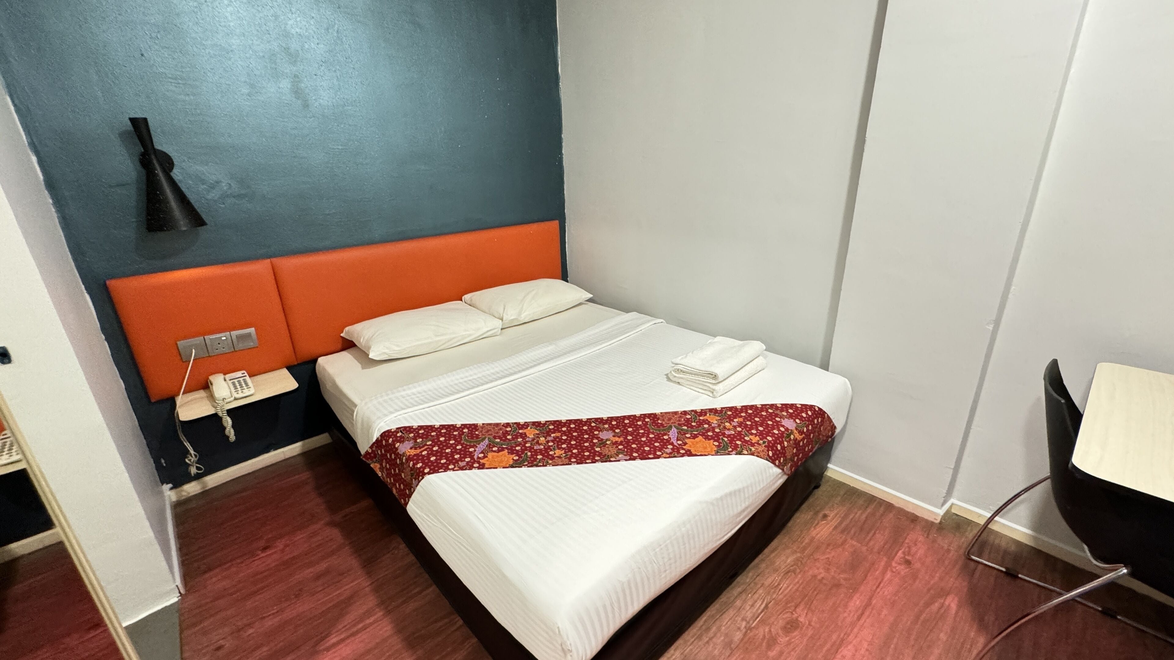 Habitación de hotel con una cama, una mesita de noche con teléfono y una silla.