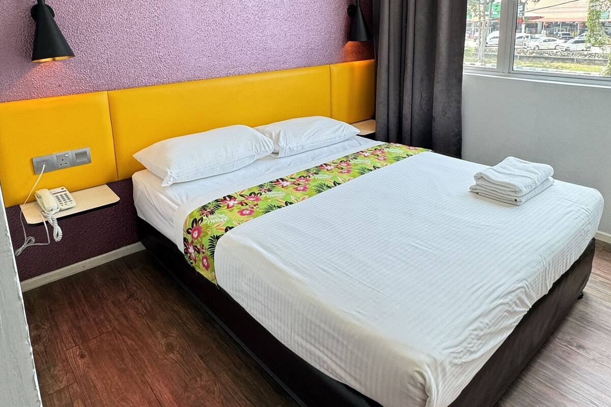 A hotel room with a bed, a telephone, a lamp, and a window with curtains.
