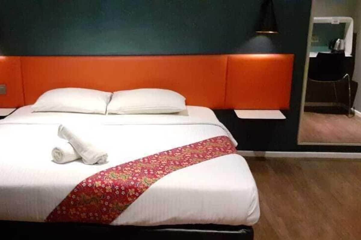 Una habitación de hotel con cama, mesita de noche, lámpara y espejo.