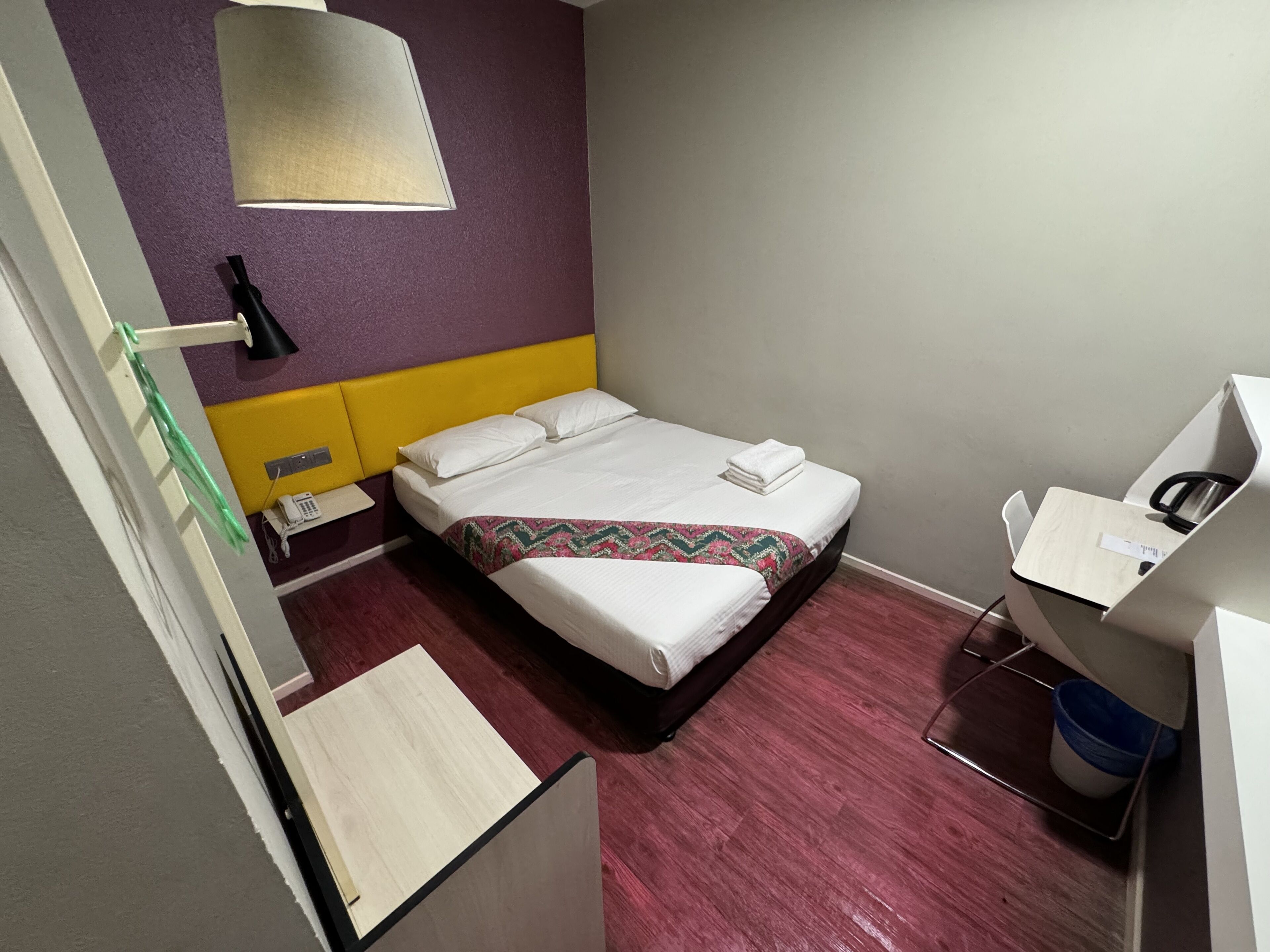 Una camera d'albergo con un letto, una scrivania, una sedia, un telefono e un cestino.