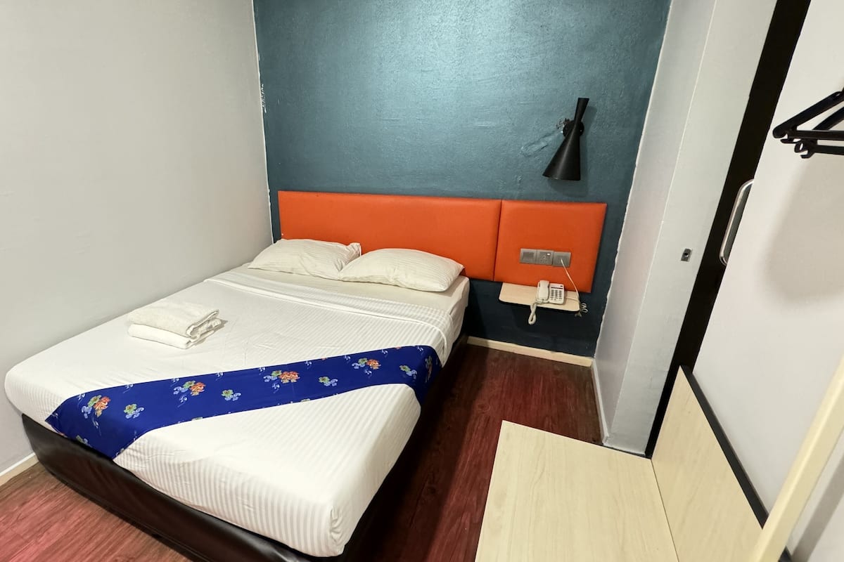A hotel room with a bed, a telephone, and a wall-mounted light fixture.