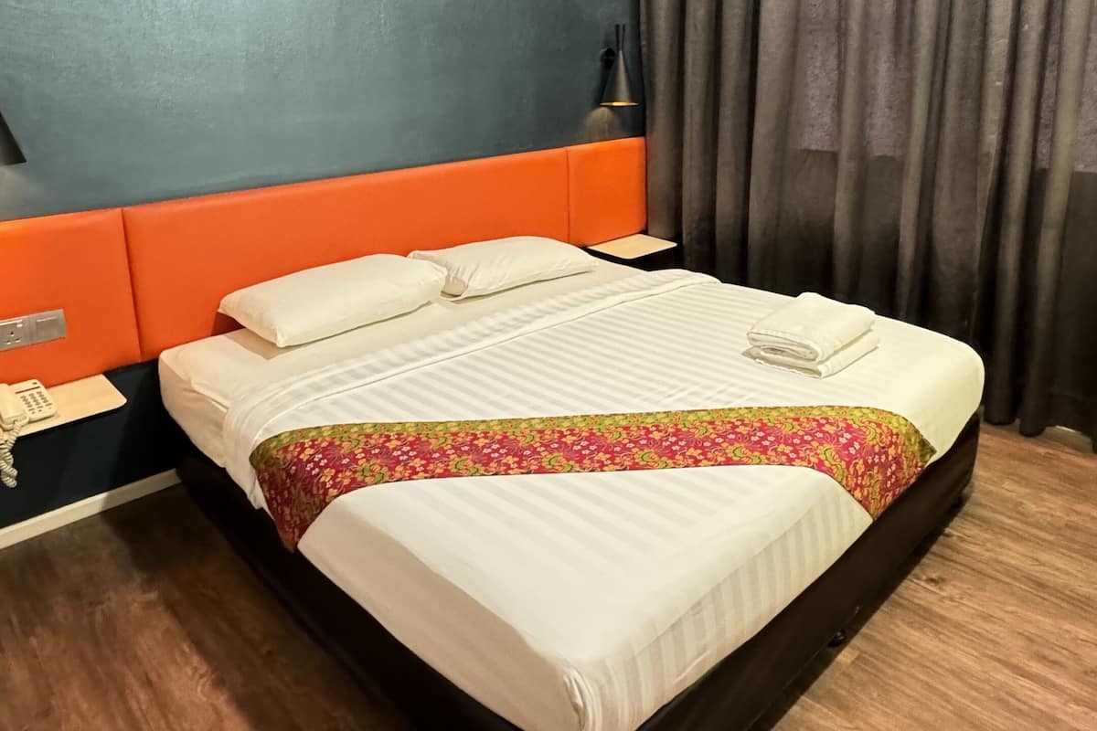 A hotel room with a bed, a nightstand, a lamp, and a window with curtains.