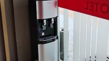 Een waterdispenser met een welkomstbord, gelegen nabij een glazen deur met een rood bord.
