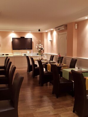A dining area with a long table, multiple chairs, a flat-screen TV mounted on the wall, and a vase with flowers on the table. - Hotel Mediterraneo (Giugliano in Campania)