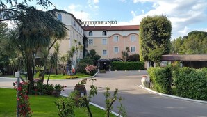 Ein Hotel mit mediterranem Namen, umgeben von gepflegten Gärten und einer gepflasterten Auffahrt.