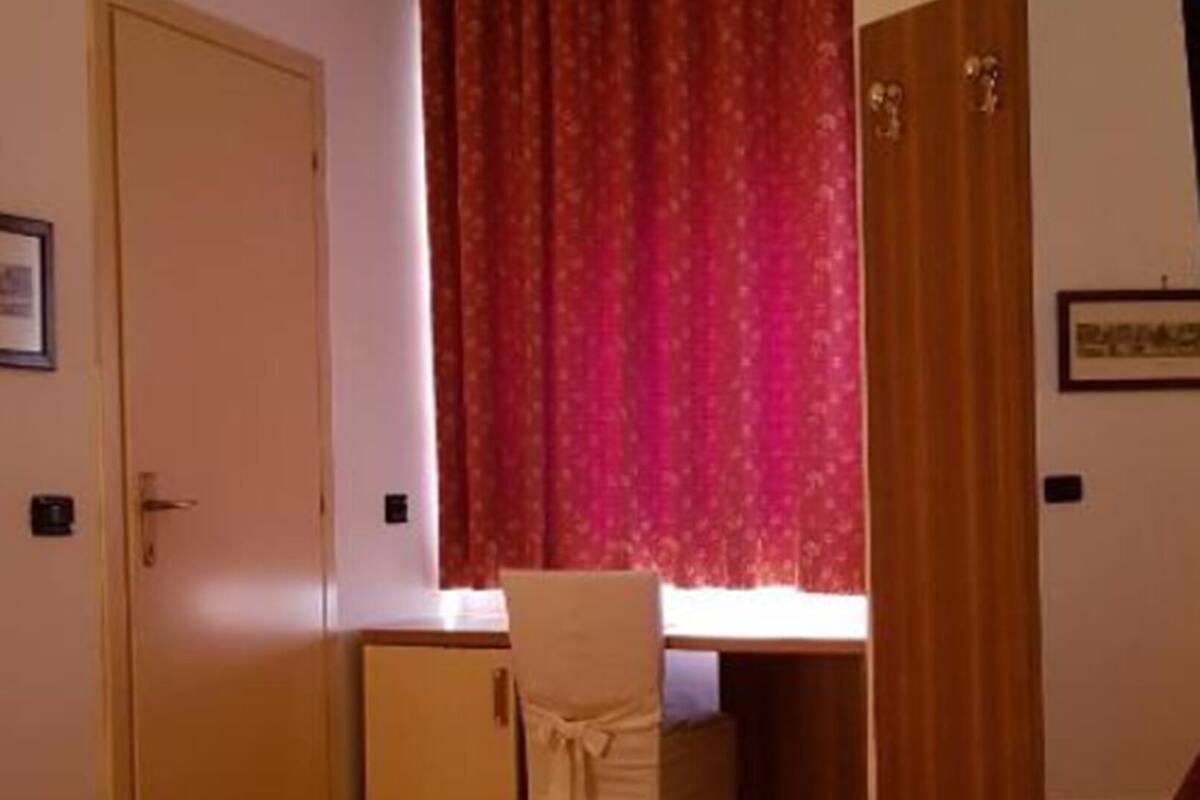A bedroom with a bed, a desk, and a window with curtains.