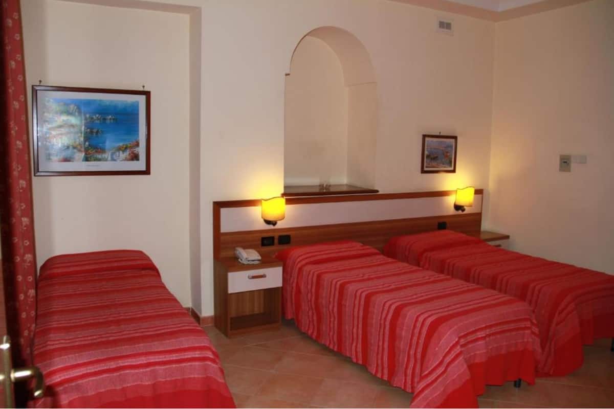 A hotel room with four single beds, a wooden headboard, a nightstand with a phone, and two wall-mounted lamps.