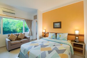 Una habitación de hotel con cama, sofá, mesita de noche y ventana con cortinas.