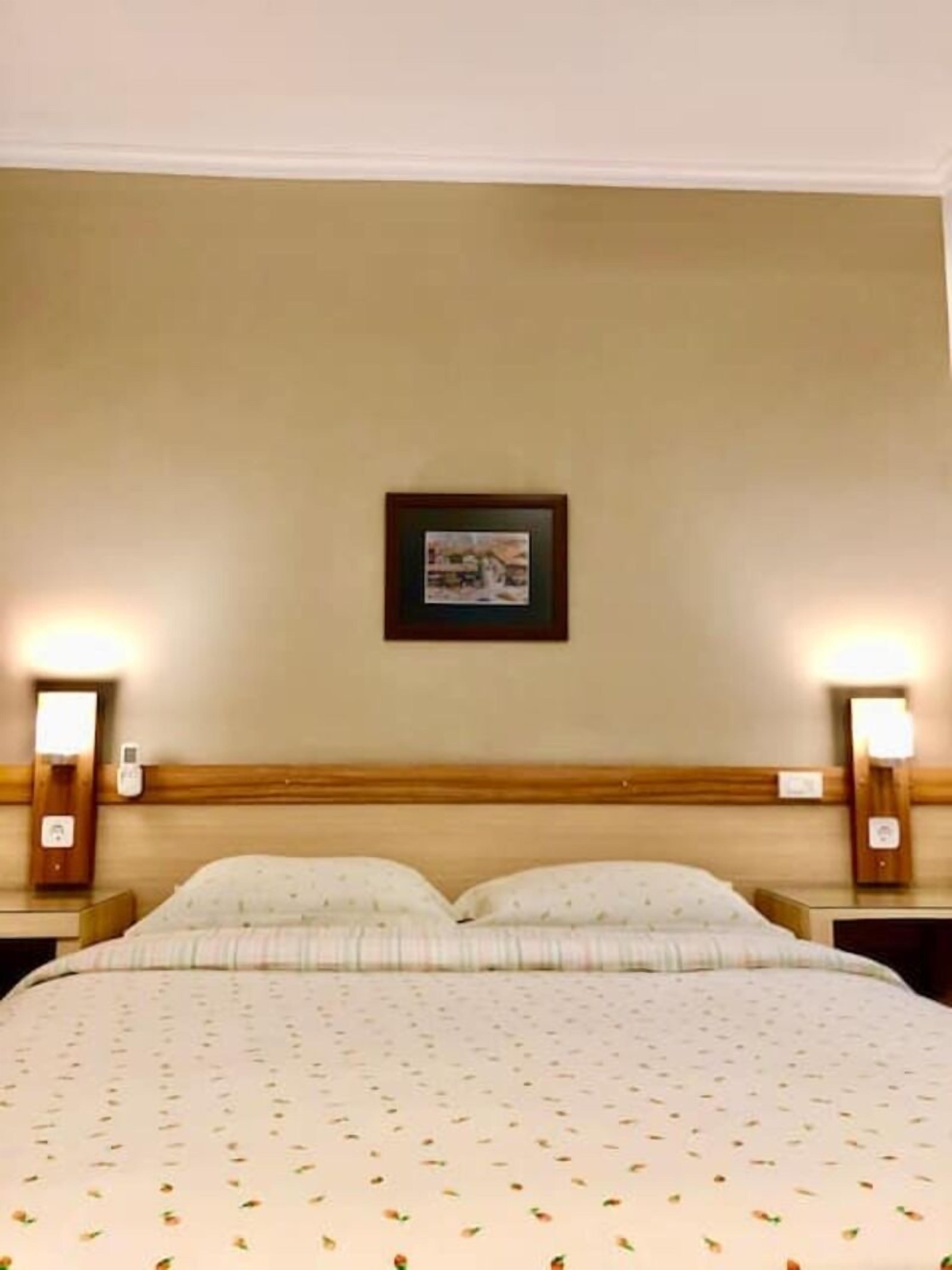 A hotel room with a large bed, two bedside tables, and a framed picture on the wall.