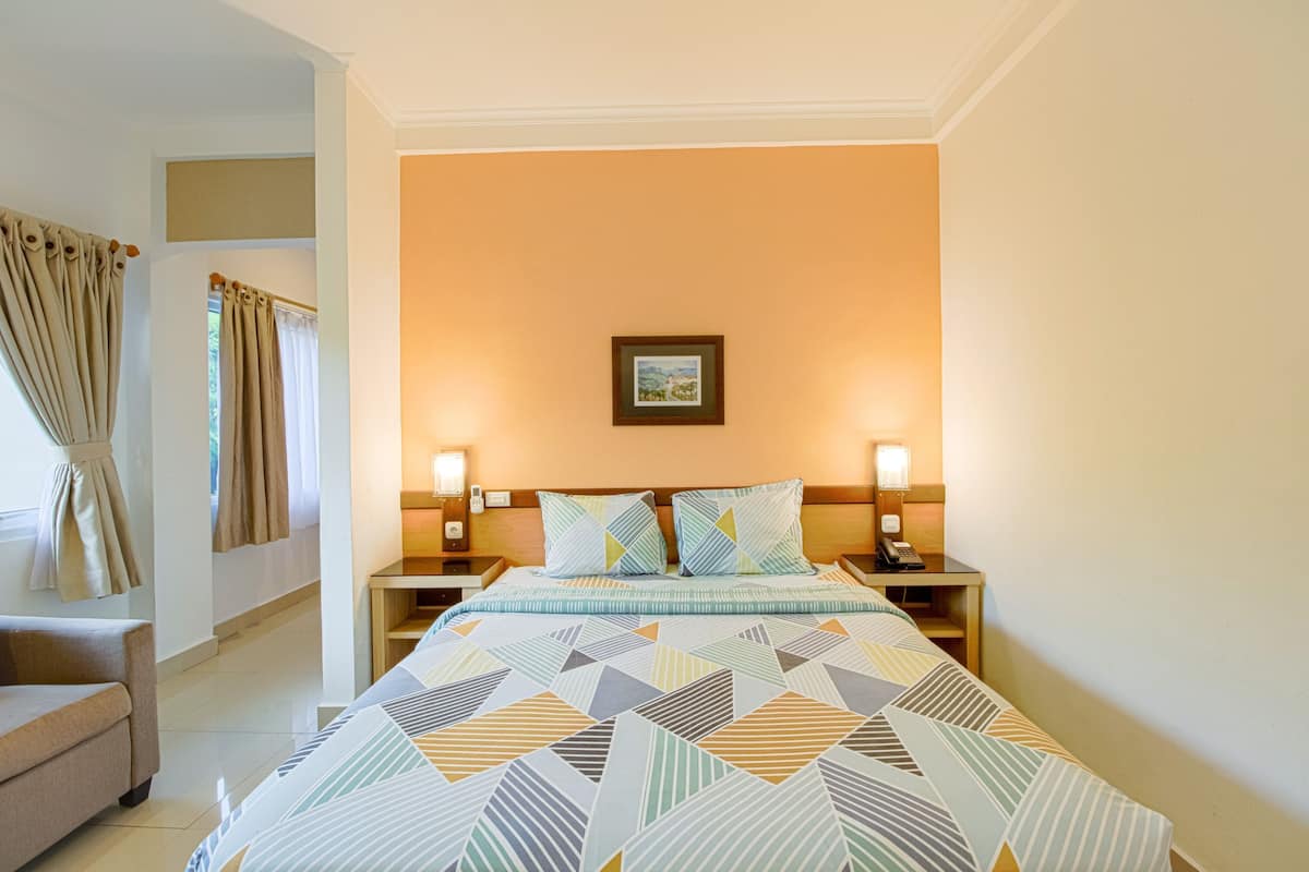 A hotel room with a bed, two bedside lamps, a nightstand, a sofa, and a window with curtains.
