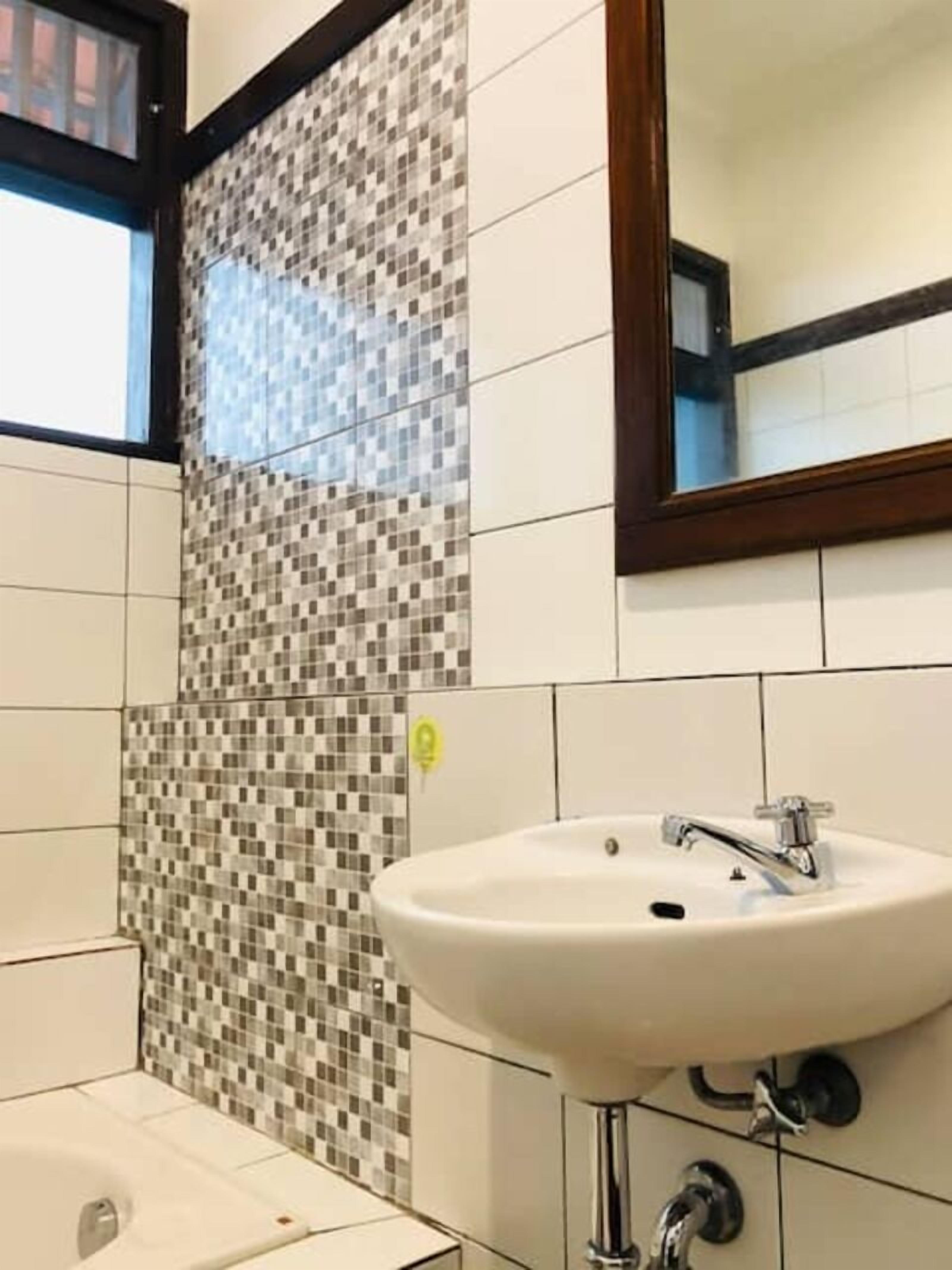 A bathroom with a tiled mosaic wall, a white sink with a chrome faucet, and a mirror above the sink.