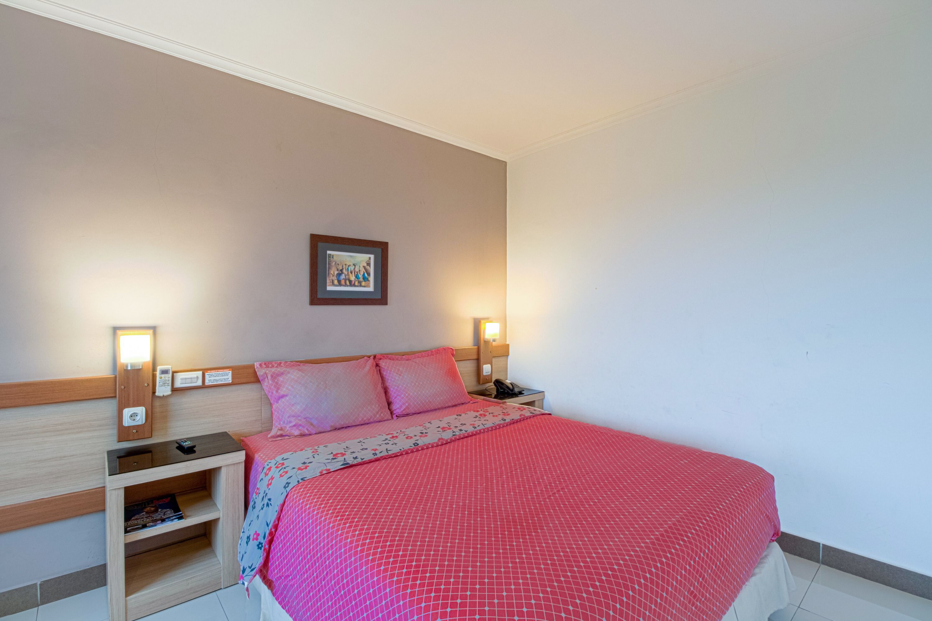 A neatly made bed with a red bedspread, a nightstand with a lamp, and a framed picture on the wall.