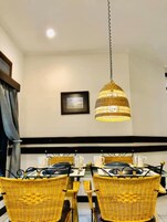 Un comedor con sillas de mimbre y una mesa, una lámpara colgante y un cuadro en la pared.