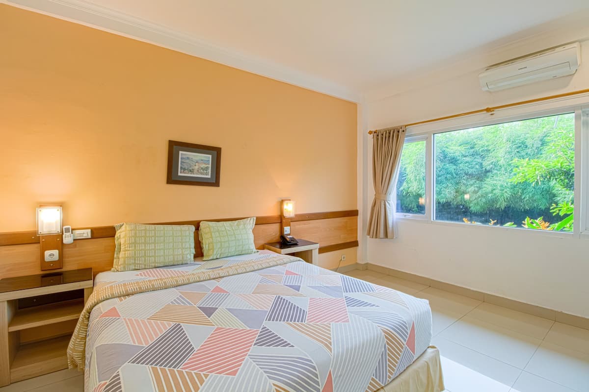 A hotel room with a large bed, bedside tables, a nightstand, a framed picture on the wall, and a window with curtains.